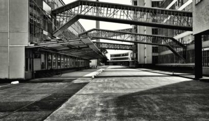Vue en noir et blanc d’un ancien bâtiment industriel avec passerelles aériennes métalliques reliant les différentes parties de l’usine.