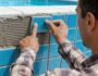 un homme pose des carreaux bleus sur le mur d'une piscine.