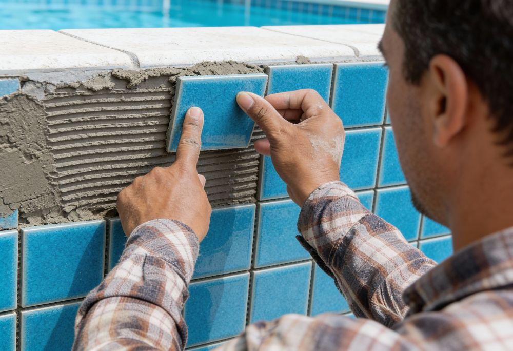 un homme pose des carreaux bleus sur le mur d'une piscine.