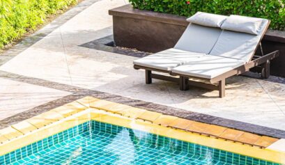 Piscine extérieure avec deux transats sur une terrasse en pierre entourée de végétation