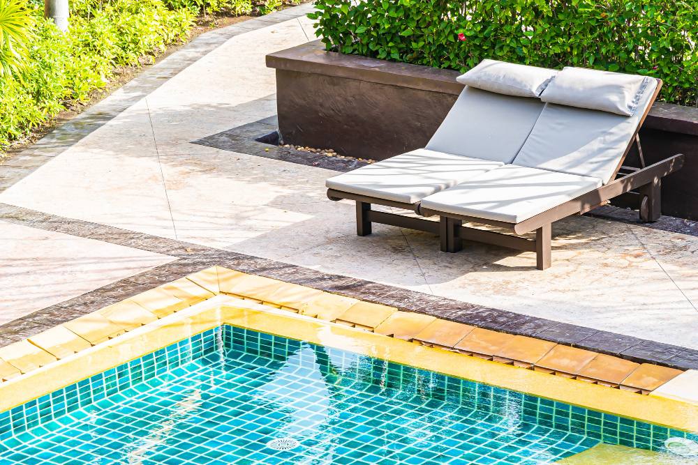 Piscine extérieure avec deux transats sur une terrasse en pierre entourée de végétation